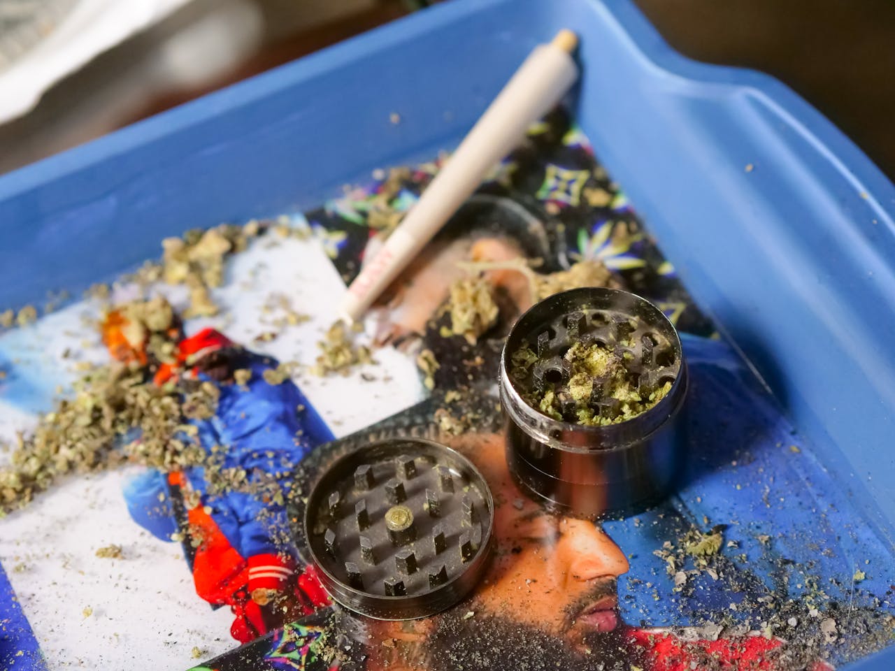 heros-img Cannabis grinder filled with marijuana next to a rolled joint on a colorful tray. Perfect for cannabis culture imagery.